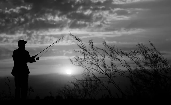 Рыбак, стоя с удочкой у реки на фоне растений и красивой облачное небо, закат и лучи света черного и белого Лицензионные Стоковые Фото