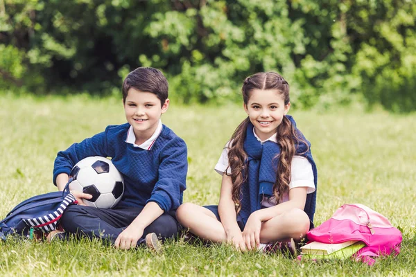 Счастливый Школьников Сидя Траве Парке Рюкзаками Футбольный Мяч Стоковое Фото